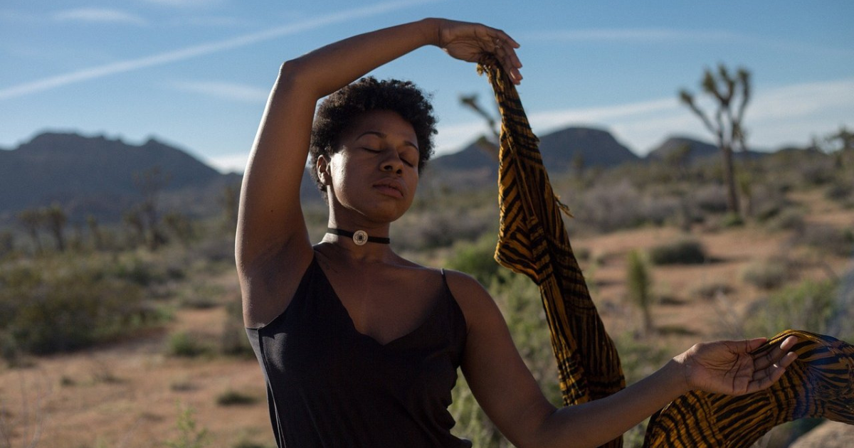 A woman sits in meditation outside in the sun.