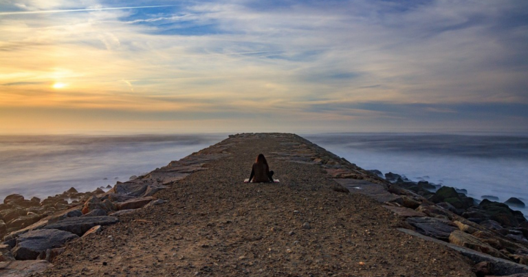 Woman meditating at sunset near the sea shore