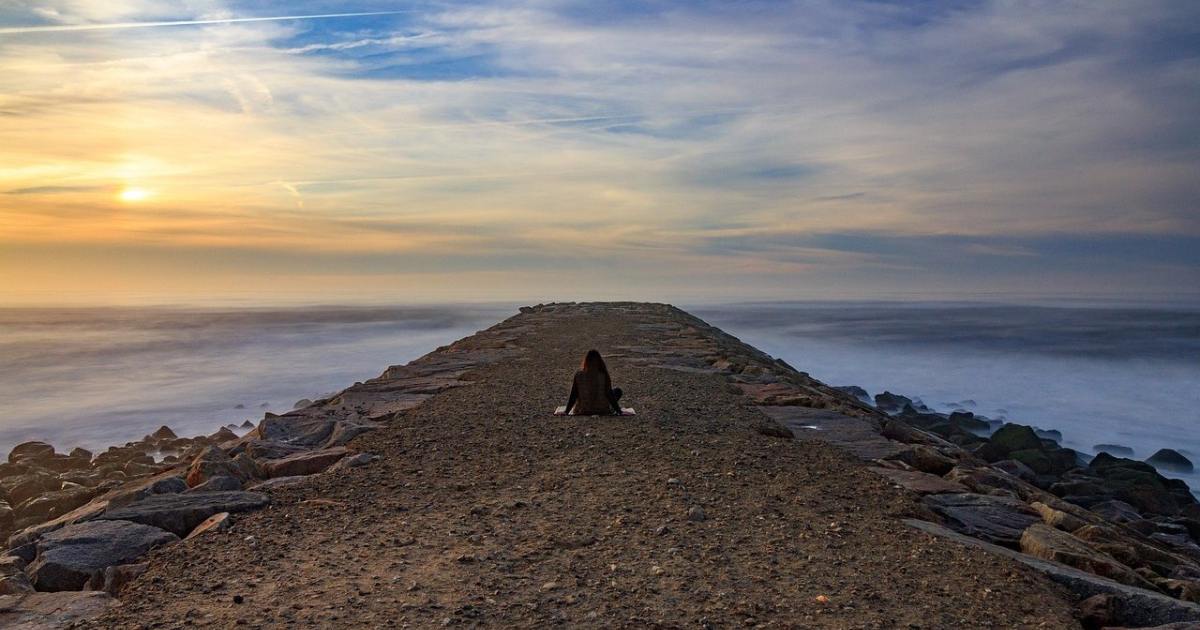 Woman meditating at sunset near the sea shore