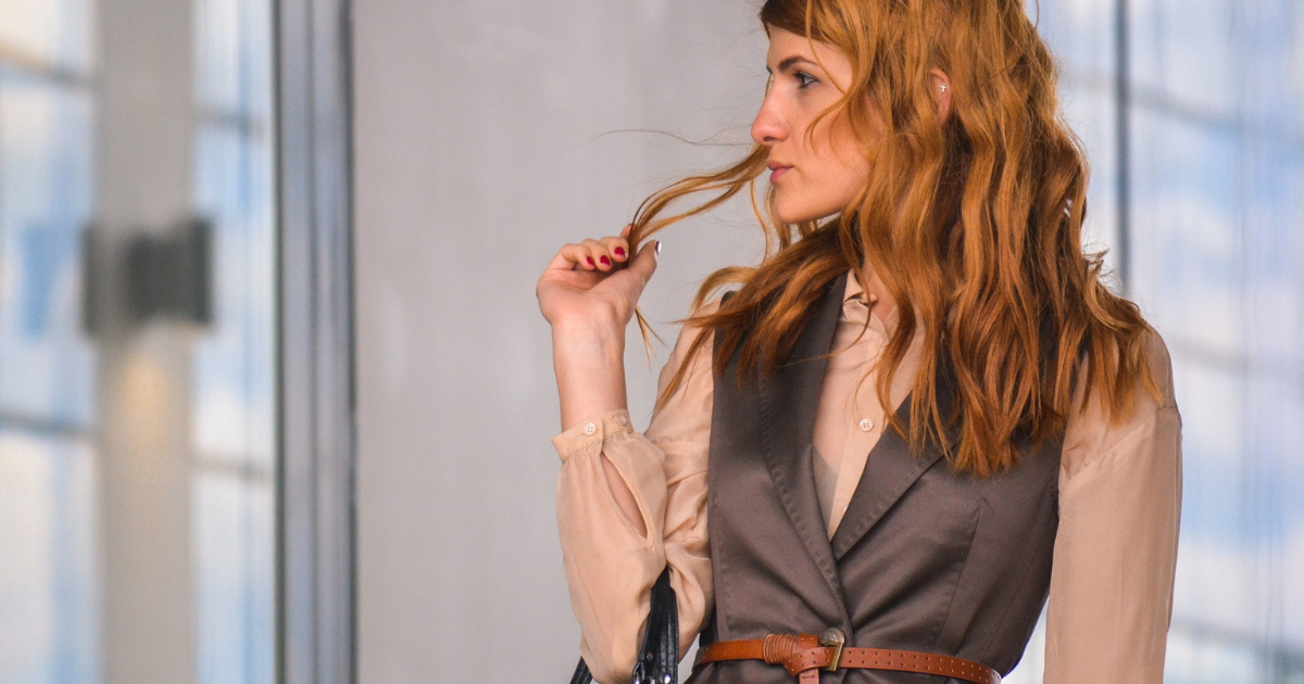 Red haired woman looking to the side and holding a strand of her hair